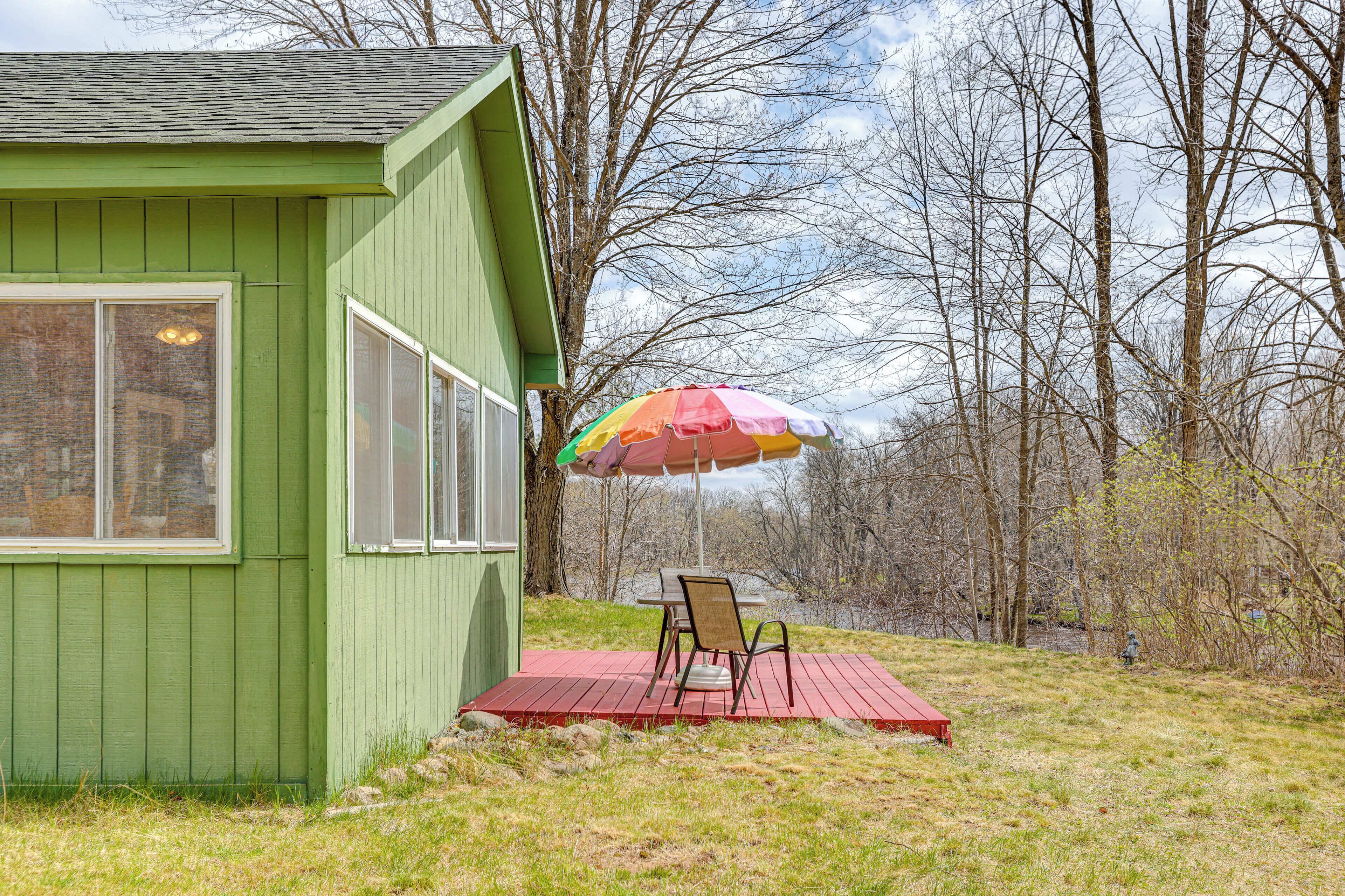 A green building with a red deck, a table with chairs, and a colorful umbrella.