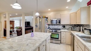 Cozinha moderna com bancada de mármore, eletrodomésticos de aço inoxidável e vista para a sala de estar.