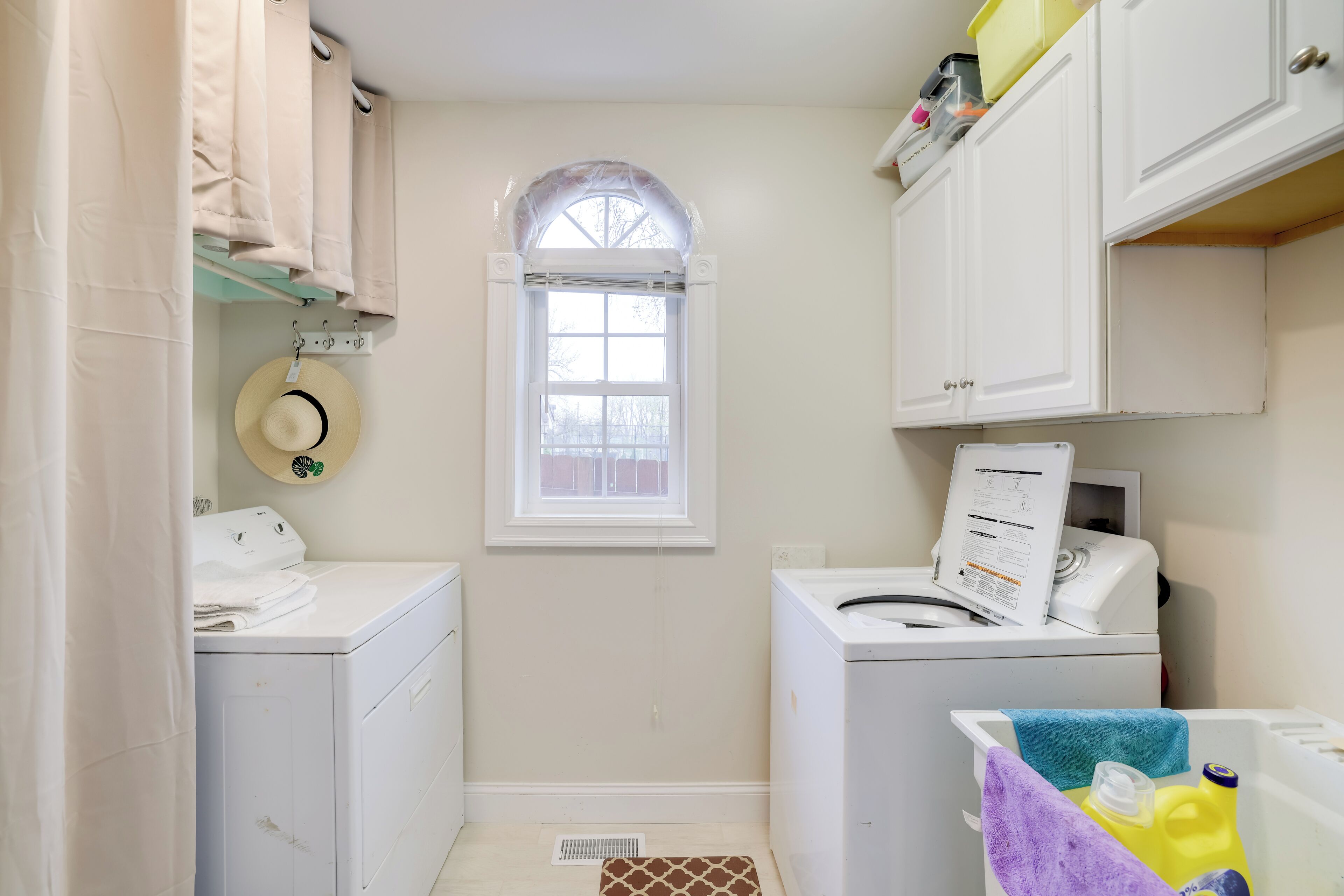 Une buanderie avec une fenêtre, un lave-linge, un sèche-linge et une étagère contenant des produits de lessive.