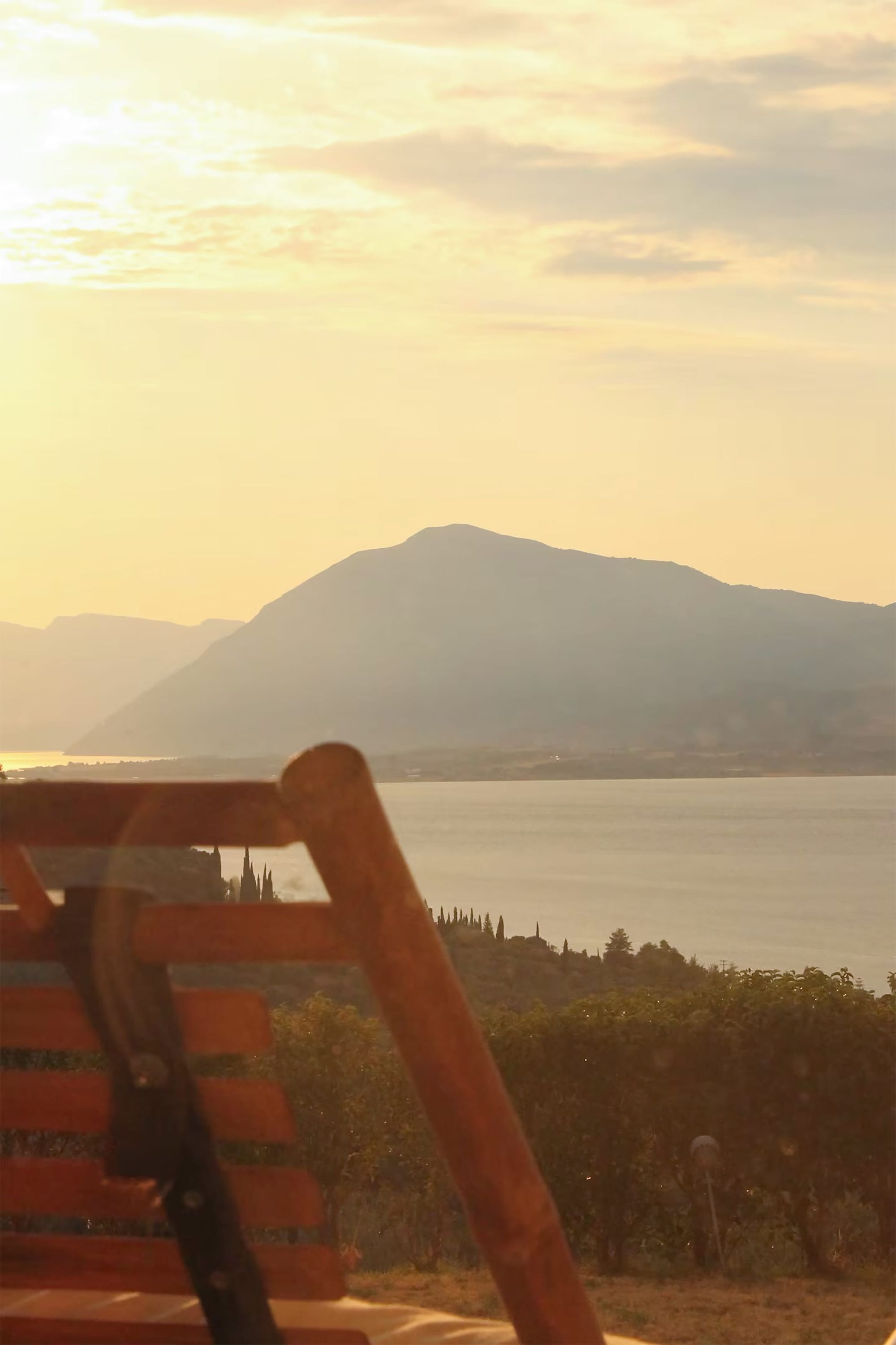 A wooden chair with a metal frame, a vineyard in the foreground, and a mountain range in the background.