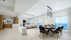 A modern kitchen with white cabinets, a marble countertop, and a dining area with a table and chairs. - Beachfront Achillion Bay Villa in Corfu (Corfu)