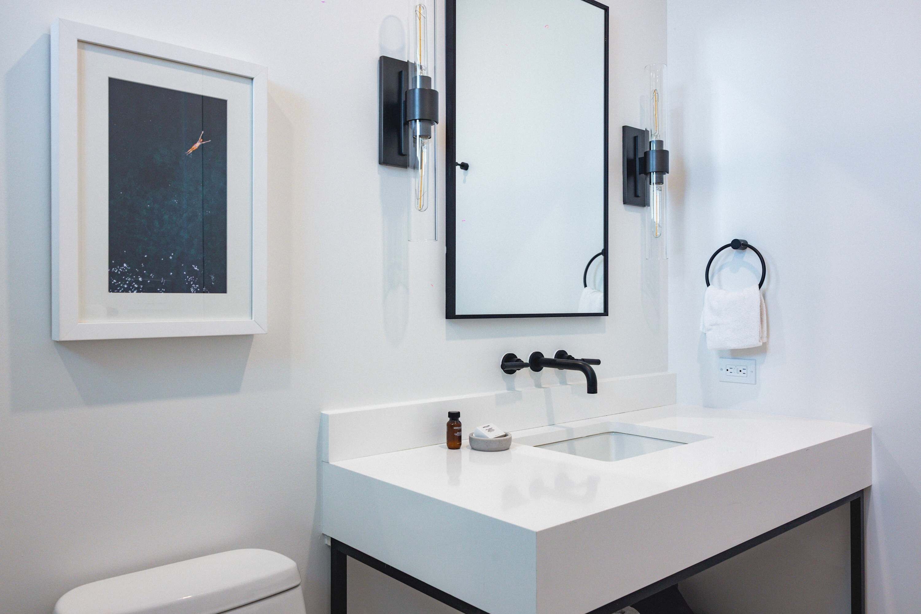 A modern bathroom with a white sink, black faucet, and a framed artwork above the mirror.