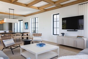 A modern living room with a white coffee table, a TV on the wall, and a dining area with wooden chairs and a black table. - Waterfront Luxury Home - Tidelands House (Key West)