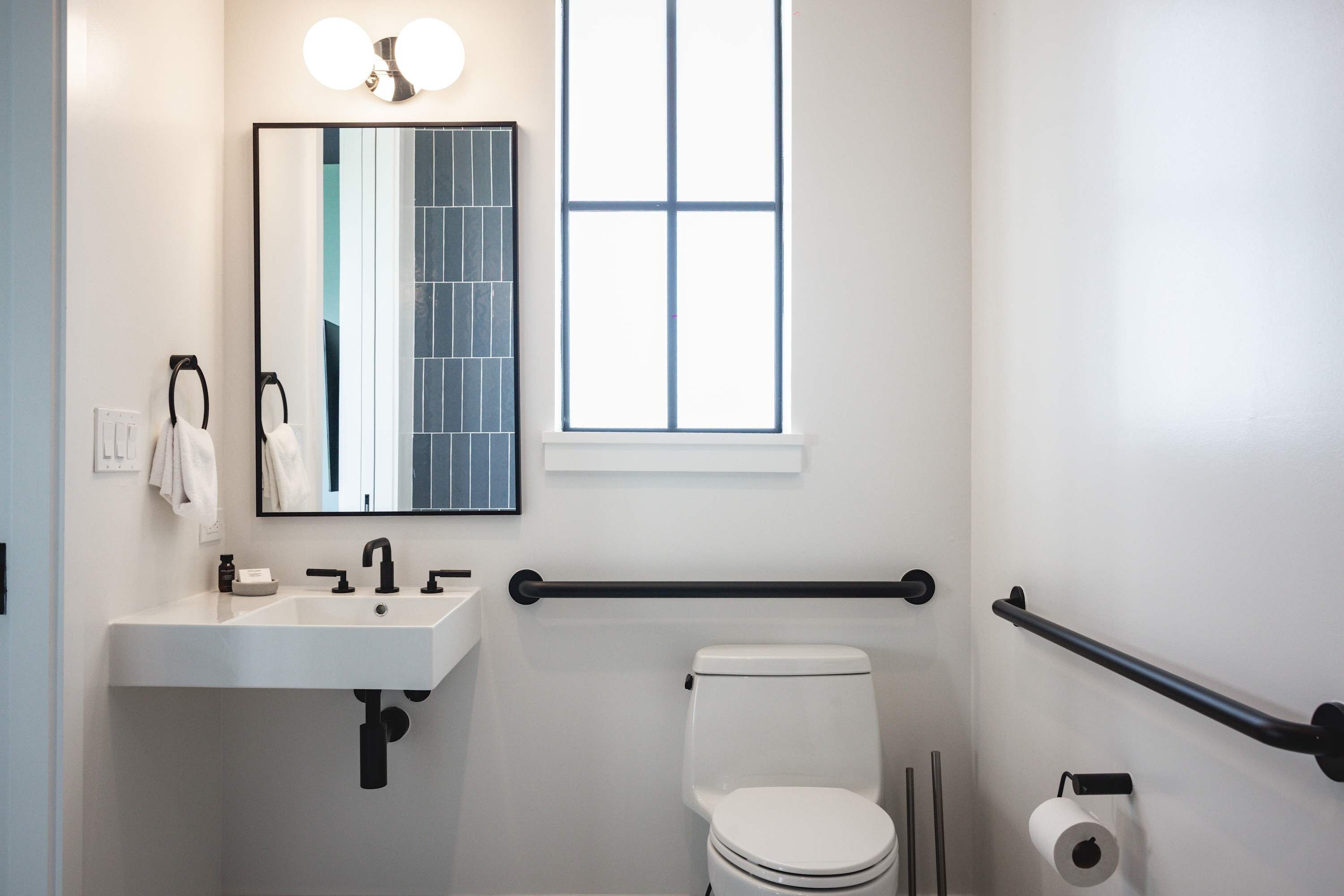 A bathroom with a white sink, a mirror, a toilet, and a window.