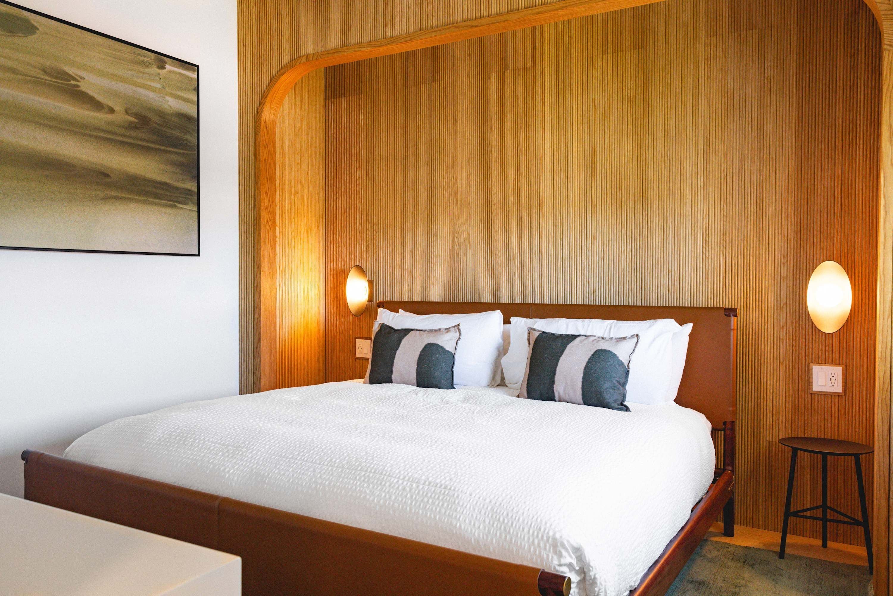 A hotel room with a large bed, wooden headboard, two wall-mounted lights, and a painting on the wall.