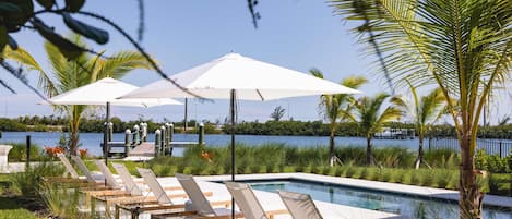 A poolside area with lounge chairs and umbrellas, a wooden deck, and a view of a body of water.