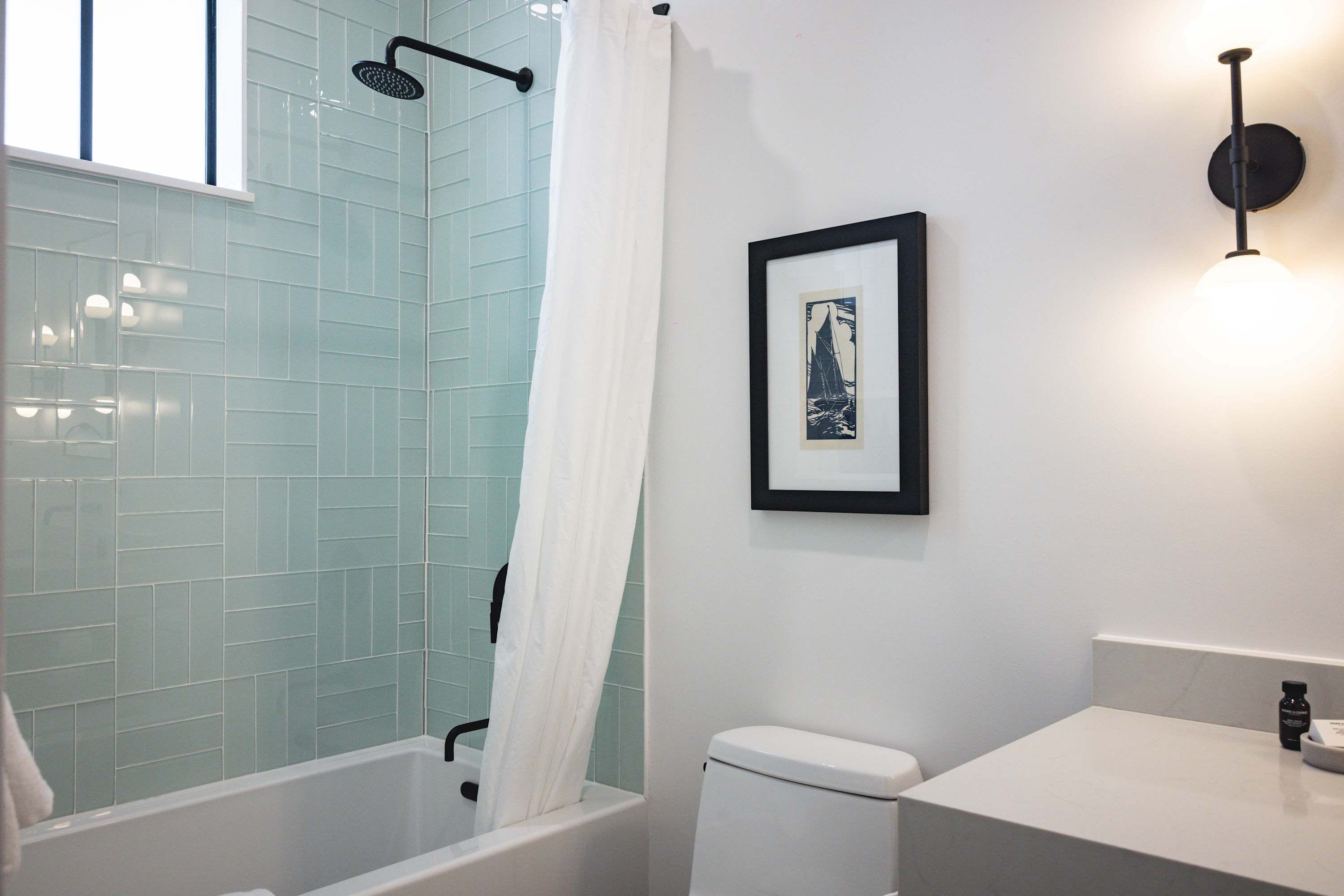 A bathroom with a shower, a toilet, a sink, and a framed picture on the wall.