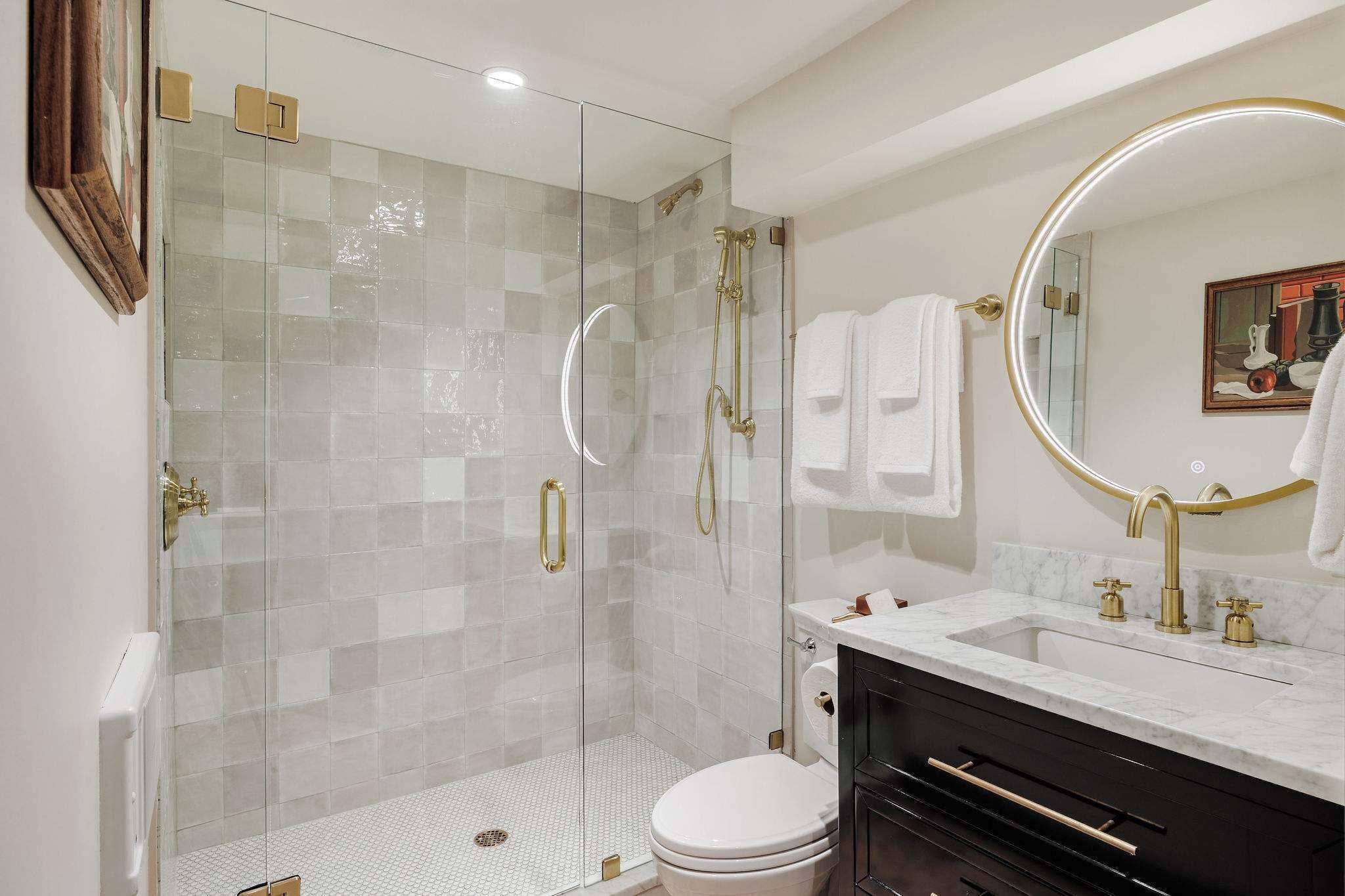 A modern bathroom with a glass-enclosed shower, a white toilet, and a vanity with a marble countertop and gold fixtures.