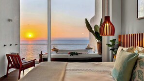 Ein Schlafzimmer mit einem großen Fenster mit Meerblick, ein Bett mit Ausblick, einer Hängelampe und einer Pflanze.