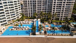 A resort with multiple swimming pools, palm trees, and a beach area.