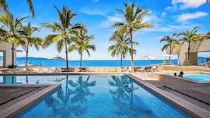 Ein Poolbereich mit Liegestühlen und Palmen, mit Blick auf das klare, blaue Meer.
