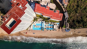 Vista aérea de un hotel costero con varias edificaciones, una playa y una zona de piscina.