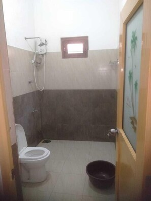 A small bathroom with a toilet, a shower, and a small window. - Golden Temple Villa  (Trincomalee)