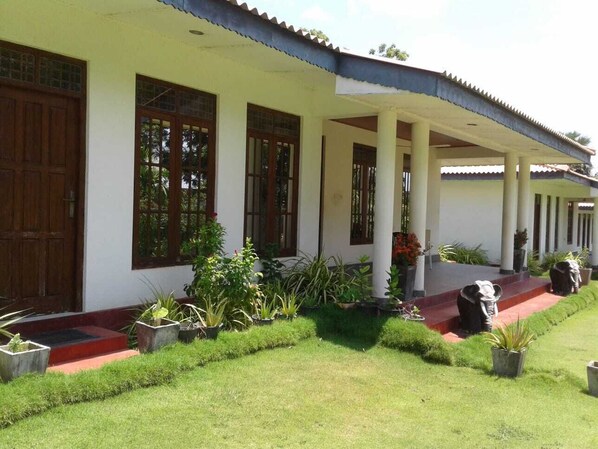 A white building with a covered porch, large windows, and a well-maintained garden with various plants and a statue. - Golden Temple Villa  (Trincomalee)