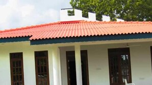 A building with a red-tiled roof, white walls, and a covered porch with white chairs. - Golden Temple Villa  (Trincomalee)