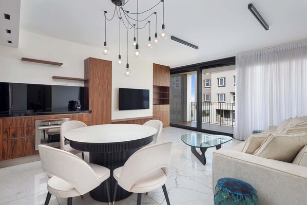 Eine moderne Küche mit Backofen, ein Essbereich mit rundem Tisch und Stühlen, ein Flachbildfernseher an der Wand und ein großes Fenster mit Blick auf die Stadt.