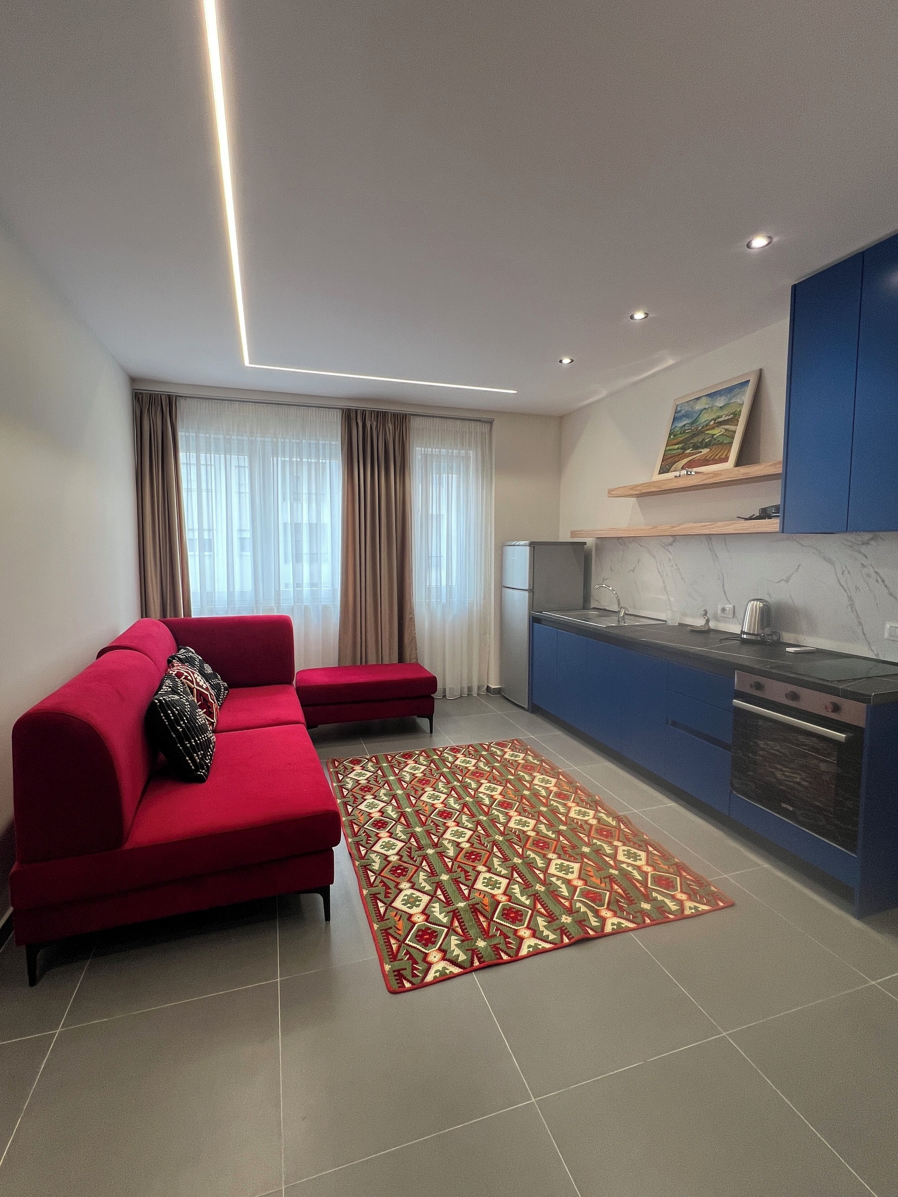 Ein modernes Wohnzimmer mit einem roten Sofa, einem gemusterten Teppich und einer Küchenzeile mit blauen Schränken.