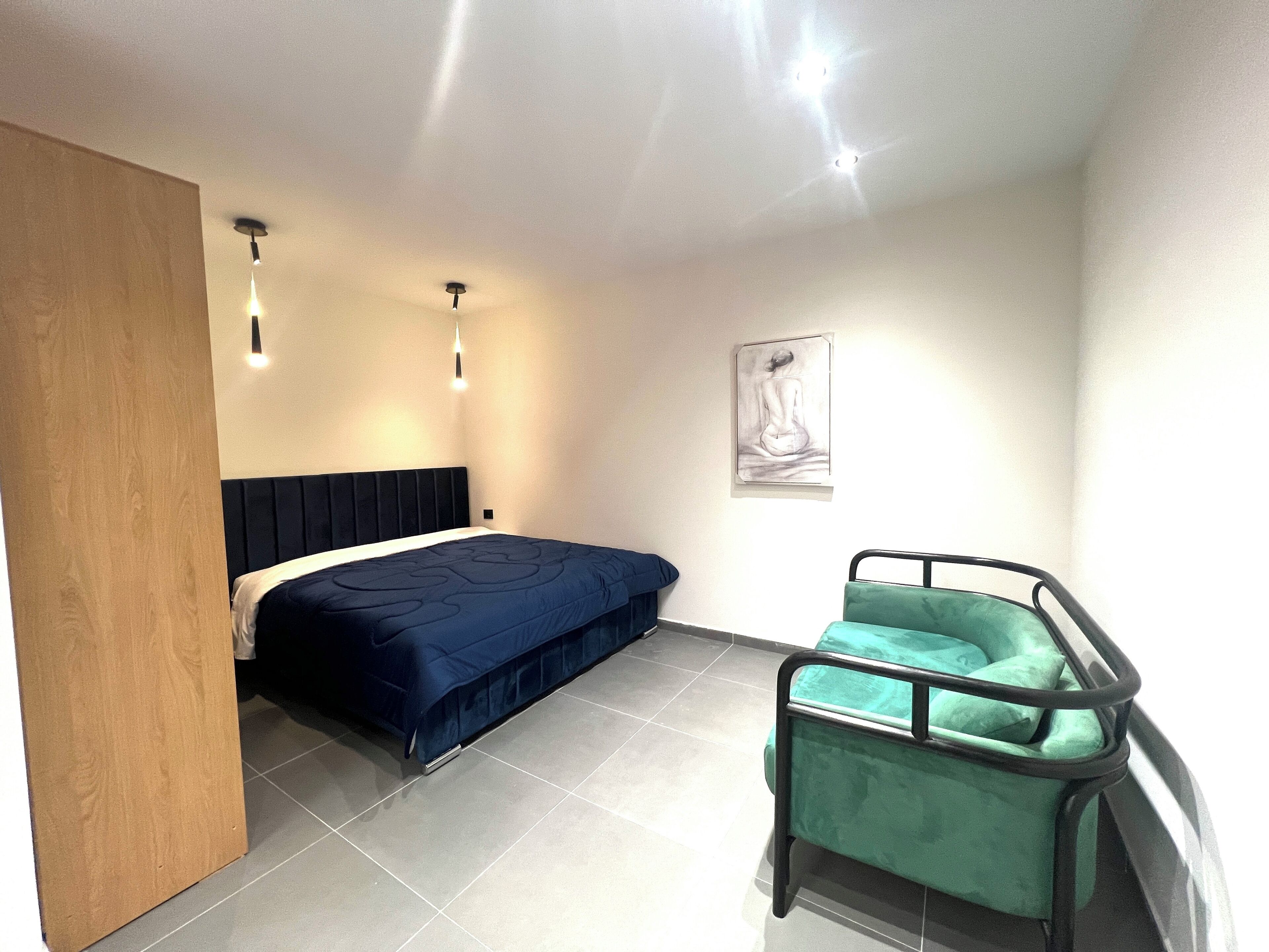 Un dormitorio moderno con una cama, una silla verde y una lámpara de techo.
