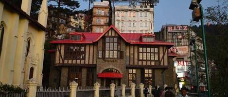 Un edificio tradicional con techo rojo y múltiples ventanas, rodeado de otros edificios y una calle.
