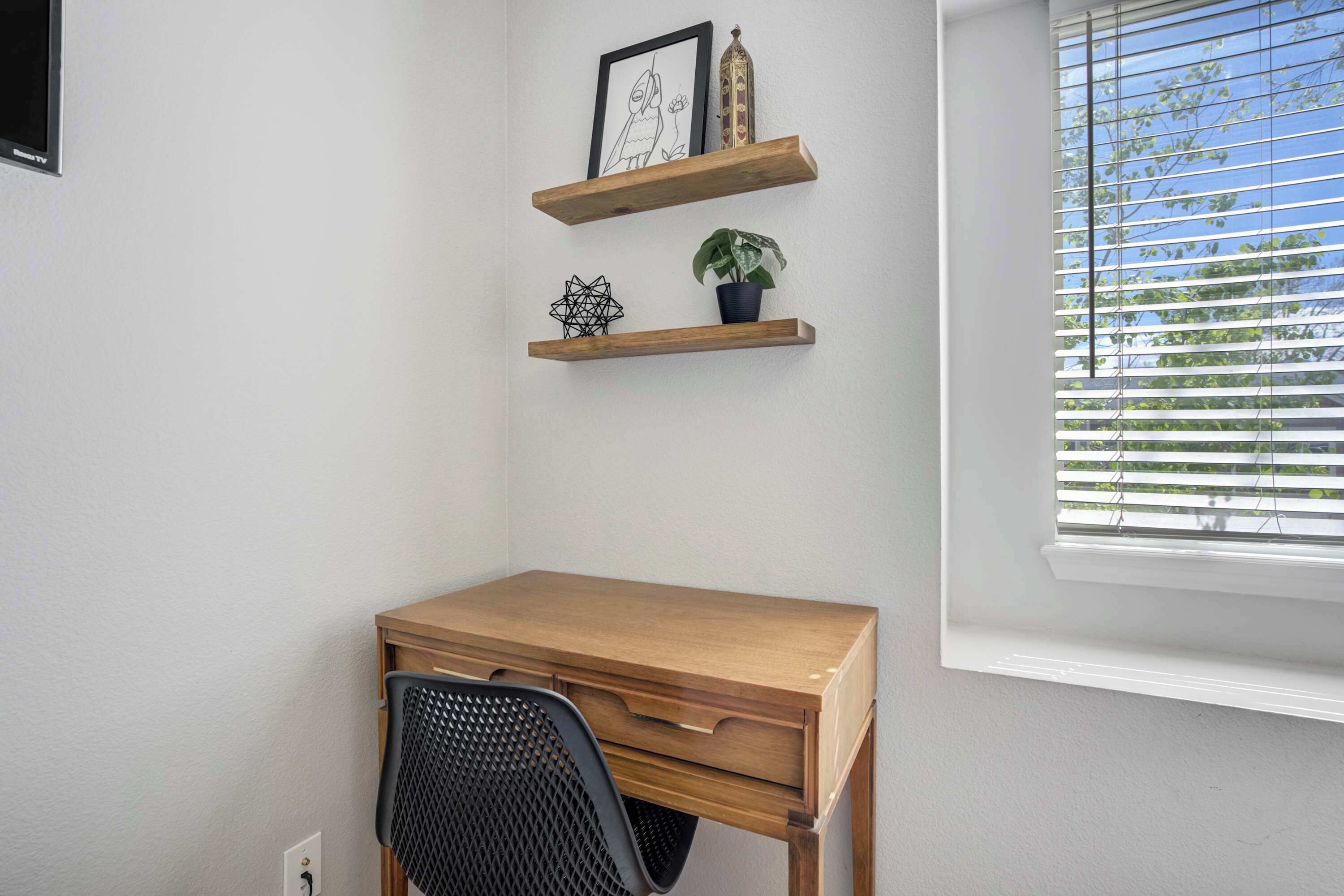 A small office space with a wooden desk, two shelves with decorative items, and a window with blinds.