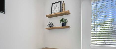 A small office space with a wooden desk, two shelves with decorative items, and a window with blinds.