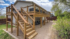 A two-story wooden deck with a staircase leading to a covered area with seating.