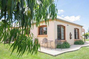 Una casa de dos pisos con un porche delantero, un comedor con sillas y mesa de metal, y un pequeño jardín.