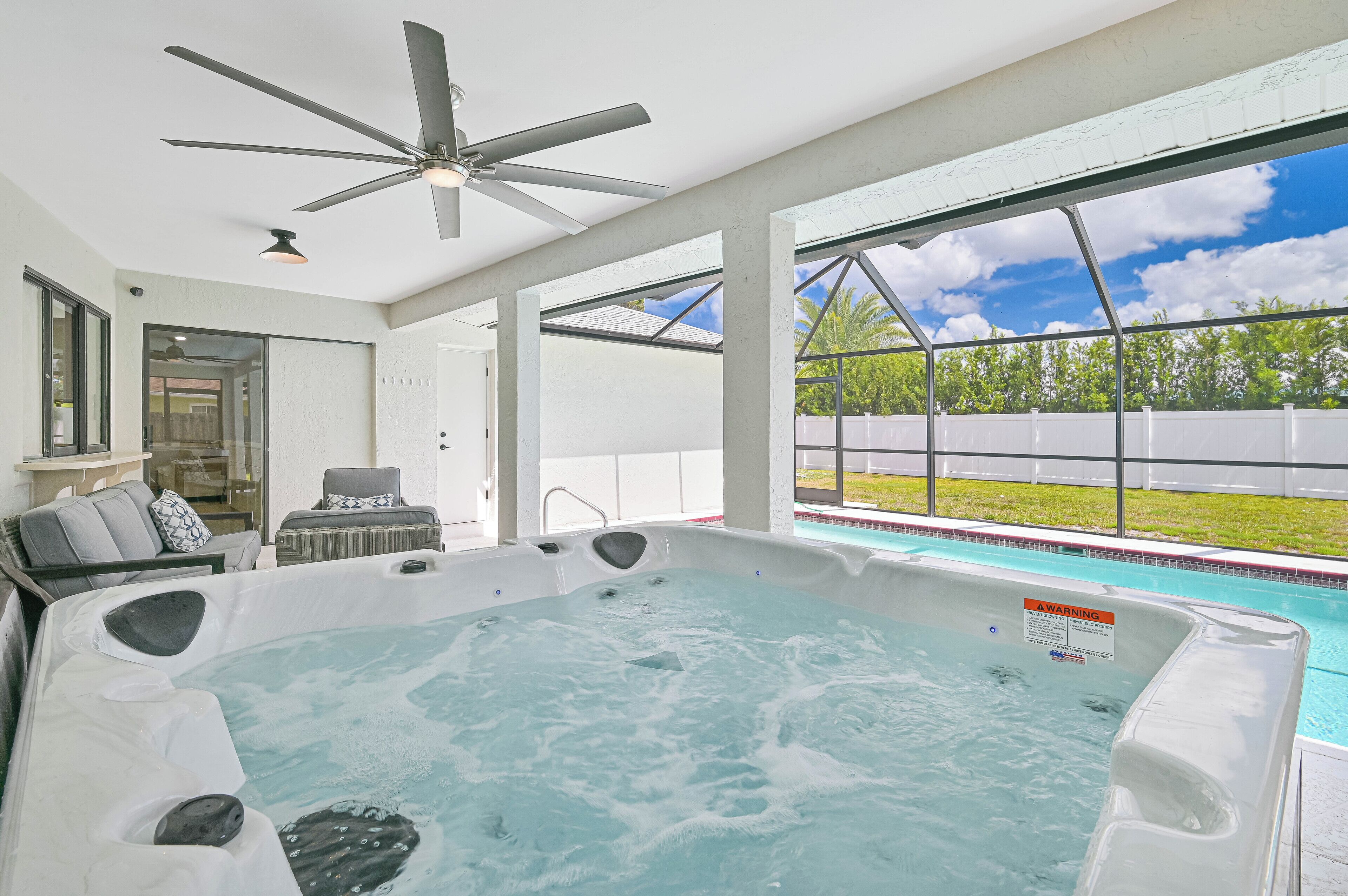 Ein moderner Poolbereich im Innenbereich mit Whirlpool, Deckenventilator und großen Fenstern mit Blick ins Freie.