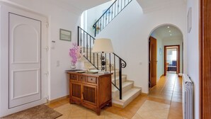 A clean, well-lit hallway with a wooden console table, a lamp, and a staircase with a black railing. - Gorgeous, family home close to Olhão, with distant sea views and a hot tub (Quelfes)