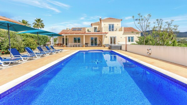 A swimming pool with lounge chairs, a patio area, and a two-story building with a tiled roof. - Gorgeous, family home close to Olhão, with distant sea views and a hot tub (Quelfes)