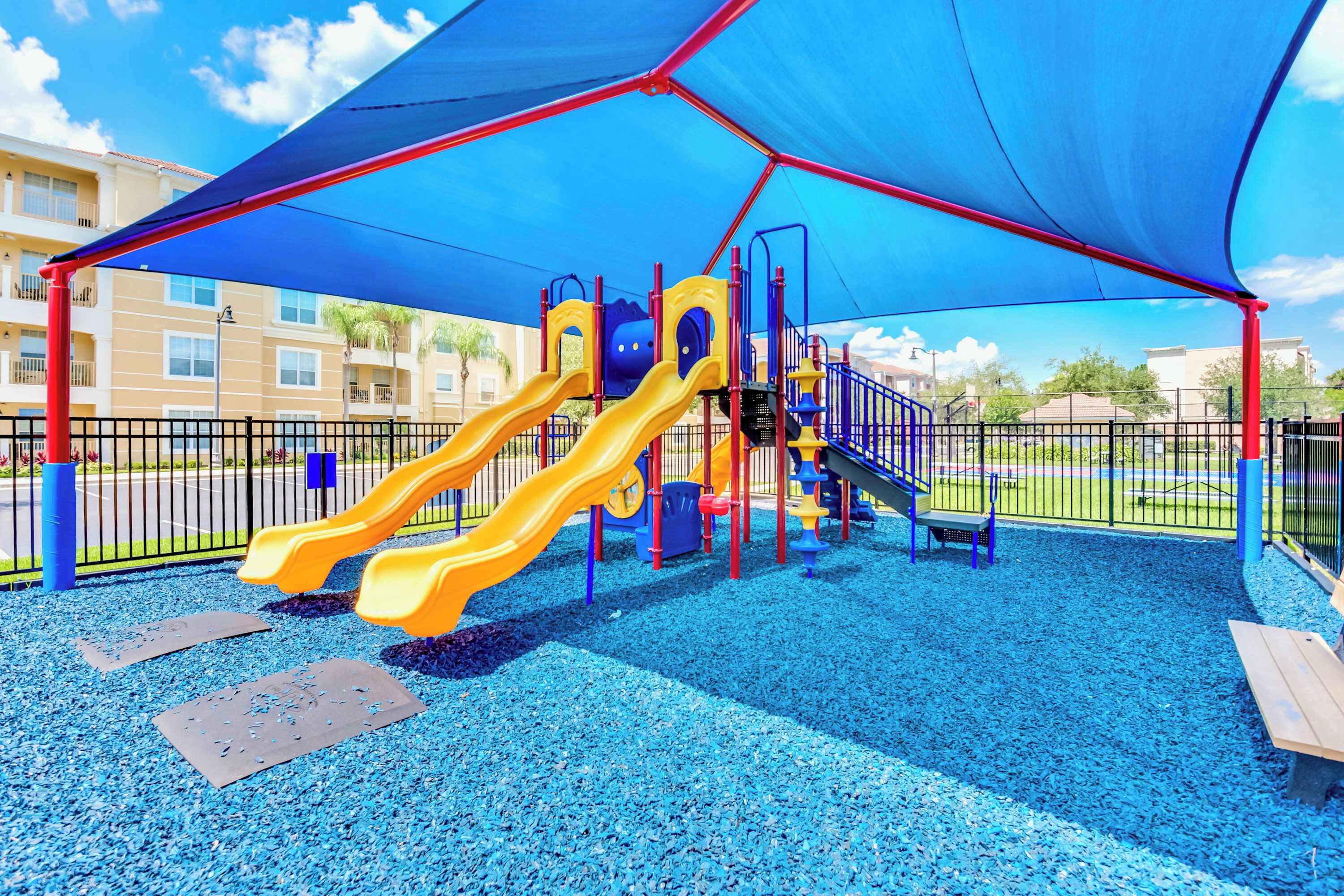 A playground with two slides, a climbing structure, and a shaded area.