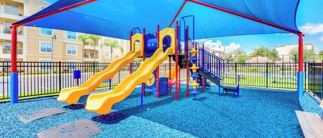 A playground with two slides, a climbing structure, and a shaded area.