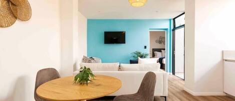 A modern living room with a round wooden table, two grey chairs, a white sofa, and a blue accent wall.