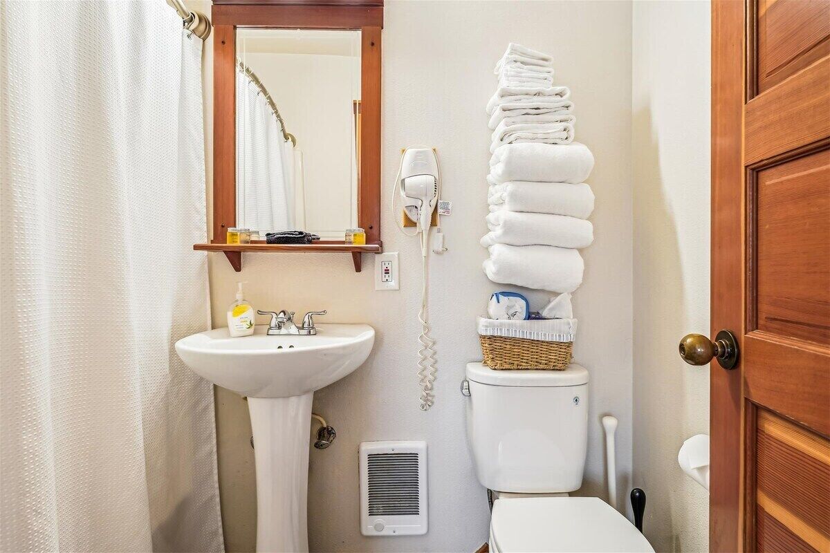 A bathroom with a white sink, a mirror, a hairdryer, and a stack of white towels.