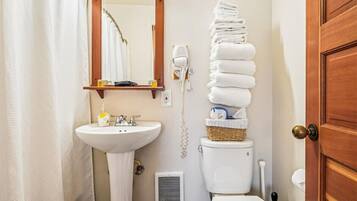 A bathroom with a white sink, a mirror, a hairdryer, and a stack of white towels.