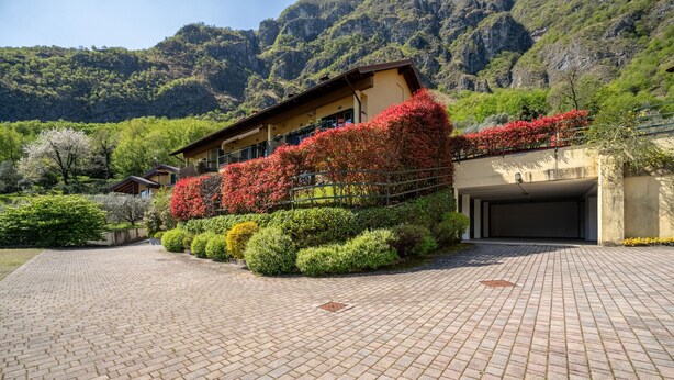 Un edificio con entrada pavimentada, rodeado de setos cuidados y plantas con flores.