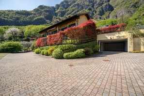 A building with a paved driveway, surrounded by well-maintained hedges and flowering plants.