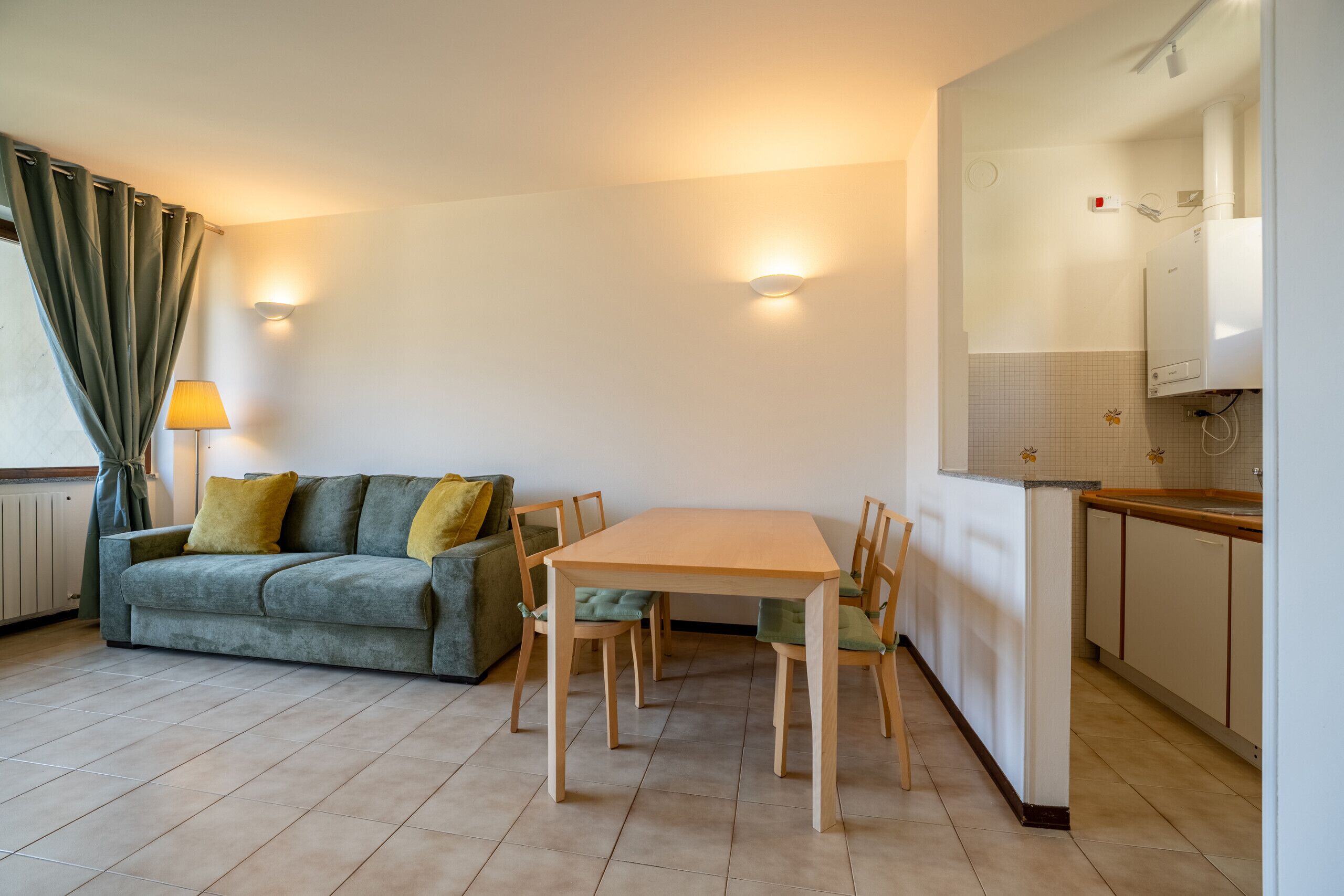 Un espacio habitable compacto con sofá, una mesa de comedor y sillas. Incluye una zona de cocina con armarios y encimera.