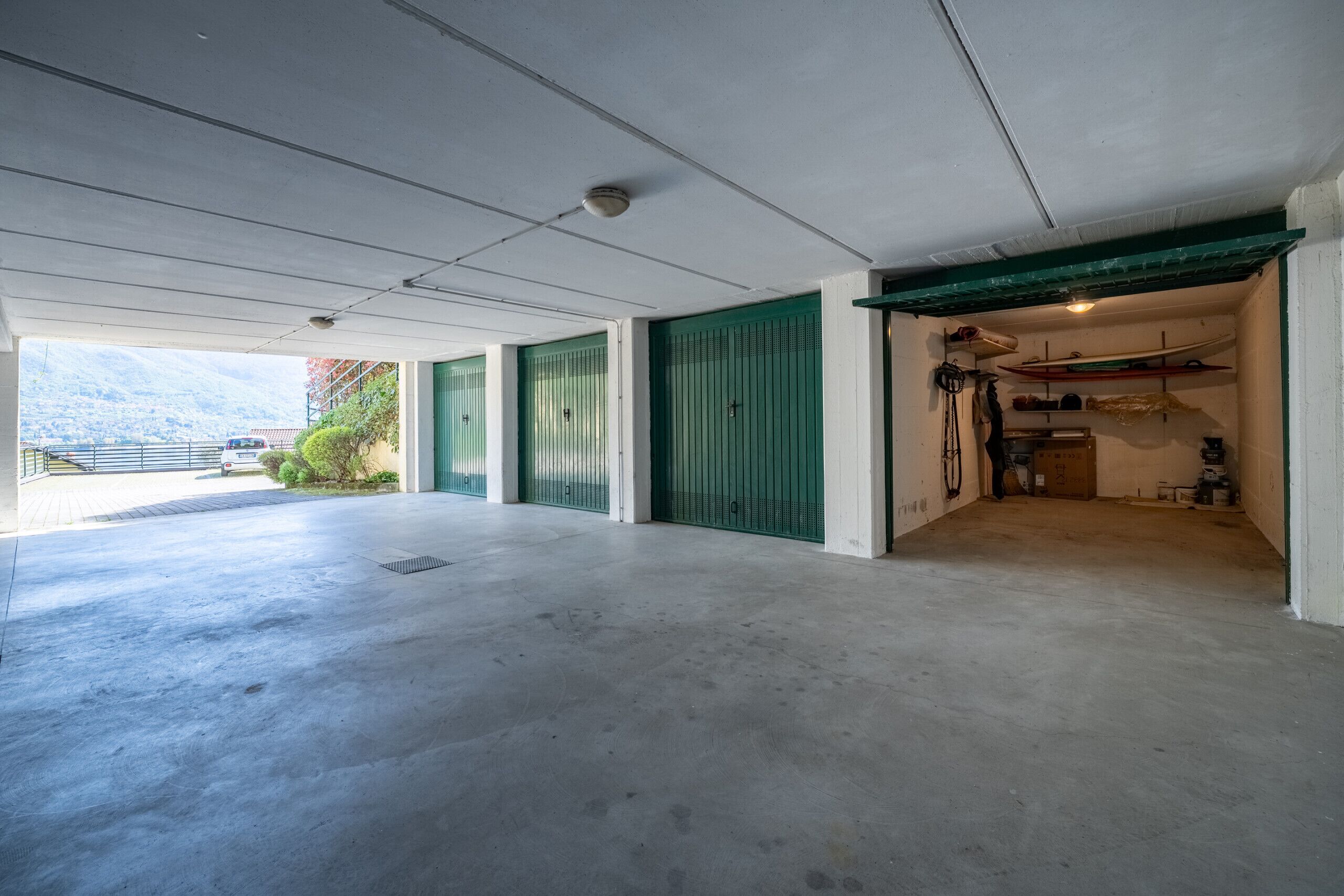 A spacious indoor area with concrete flooring, green doors, and a visible outdoor view.