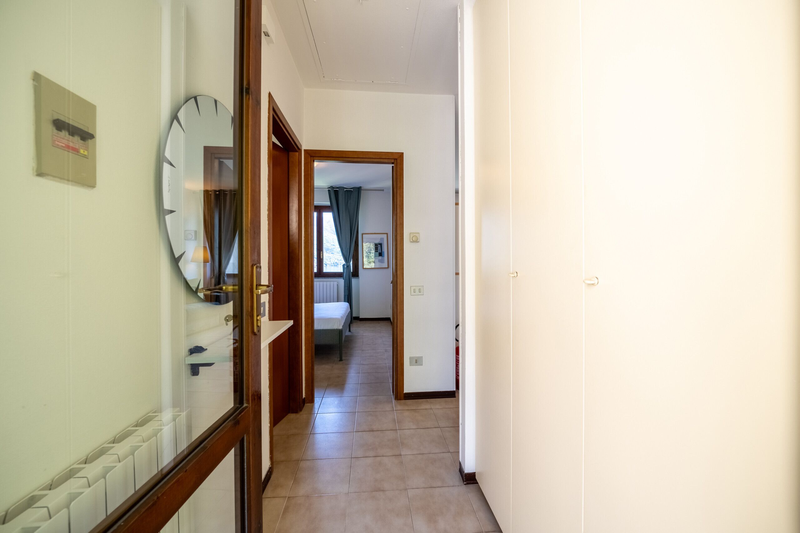A hallway with a radiator, a clock, and a door leading to a bedroom with a bed and curtains.
