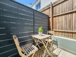 A patio area with a black fence, wooden chairs, a small table, and a potted plant. - Luminous 1-bedroom apartment with WiFi and 300m from the sea (Cape Town)