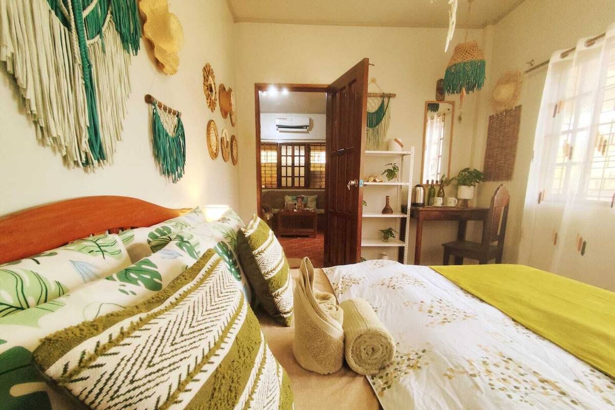 A bedroom with a bed, a desk, and a shelf with plants.
