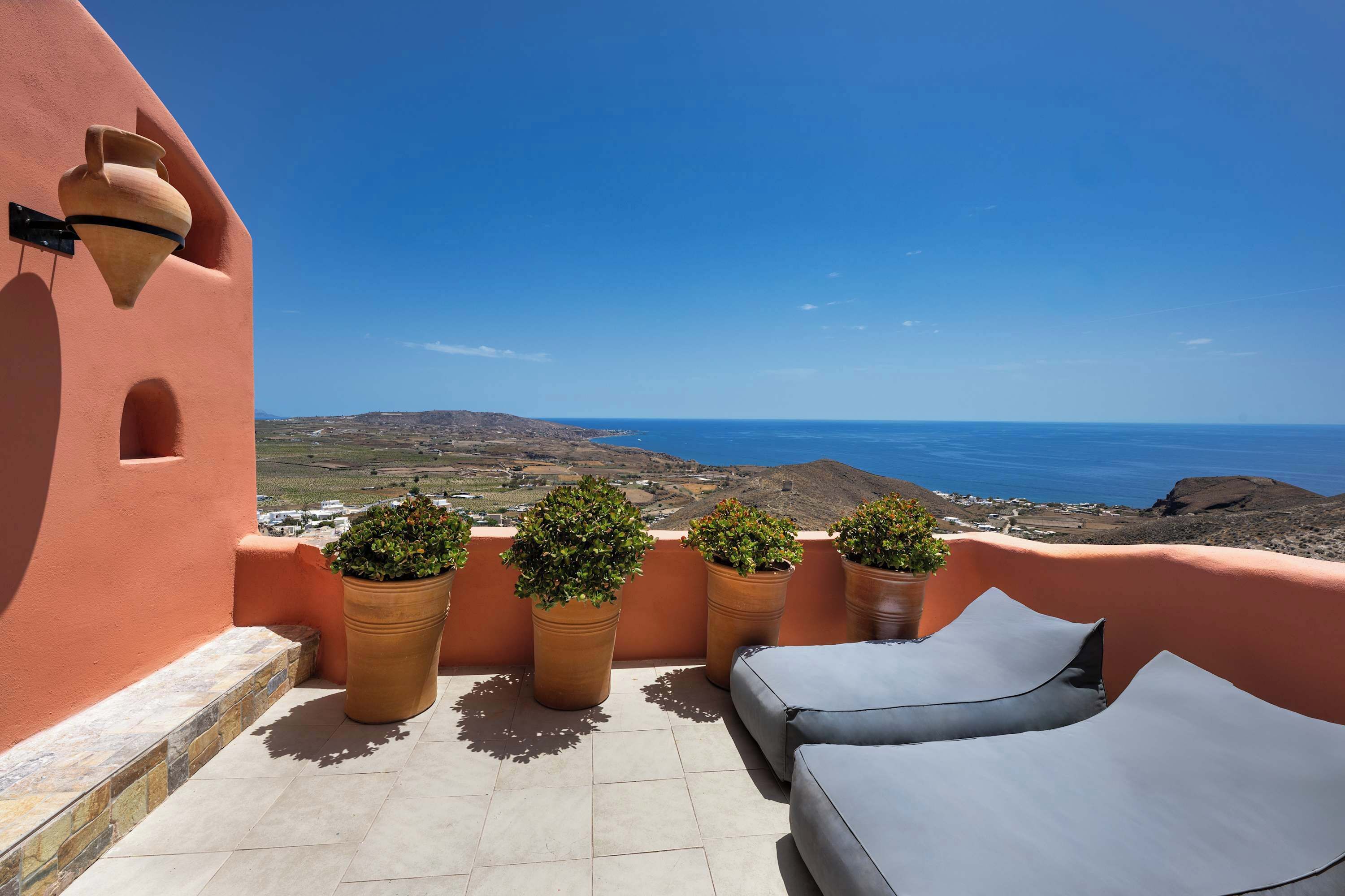 Une terrasse avec vue sur la mer, agrémentée de plantes en pot et de chaises longues.