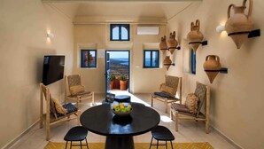 A dining area with a round table, four chairs, a bowl of fruit, and a view through an open door. - Amphora Aelia Gem - Akrotiri Seaview Getaway (Akrotiri)
