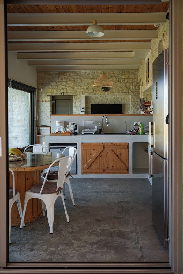 A modern kitchen with a stone wall, wooden cabinets, and a built-in dishwasher. - Oliva Emerald Eco - Secluded Off-Grid Vineyard Villa (Kato Vathia)