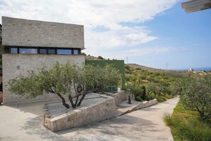 A modern building with stone walls and a pathway lined with trees. - Oliva Emerald Eco - Secluded Off-Grid Vineyard Villa (Kato Vathia)