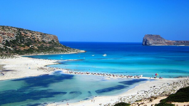 Une scène de plage côtière avec une eau d’un bleu limpide, des rivages sablonneux et des falaises rocheuses.