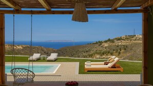 Un espace aménagé au bord de la piscine avec vue sur la mer, une table en bois sur laquelle se trouve un saladier rempli de fruits, et deux chaises longues.