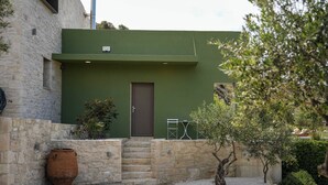 Ein Steinhaus mit grüner Fassade, einer braunen Tür und einer kleinen Außenbereich-Sitzgelegenheit mit Tisch und Stühlen.