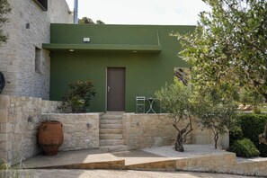Ein Steinhaus mit grüner Fassade, einer braunen Tür und einer kleinen Außenbereich-Sitzgelegenheit mit Tisch und Stühlen.